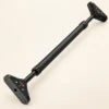 Barre de traction de porte sans vis 75-94 cm noire seule, inclinée en diagonale : tube central lisse, bagues de serrage crantées, tiges filetées et plaques d'appui à patin strié, sur fond crème